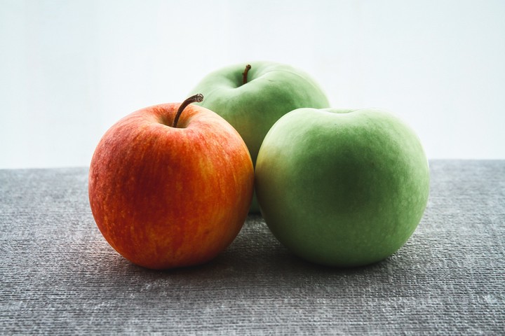 1 manzana roja y 2 manzanas verdes sobre una mesa, foto tomada por Benjamin Wong