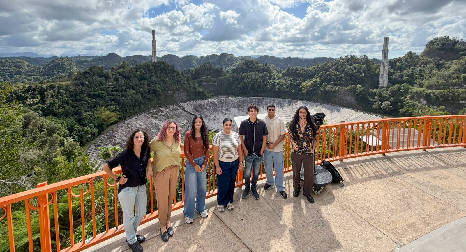 Foto grupal de docentes y estudiantes del taller en un paseo por el Observatorio Arecibo con el plato del radio telescopio de fondo.