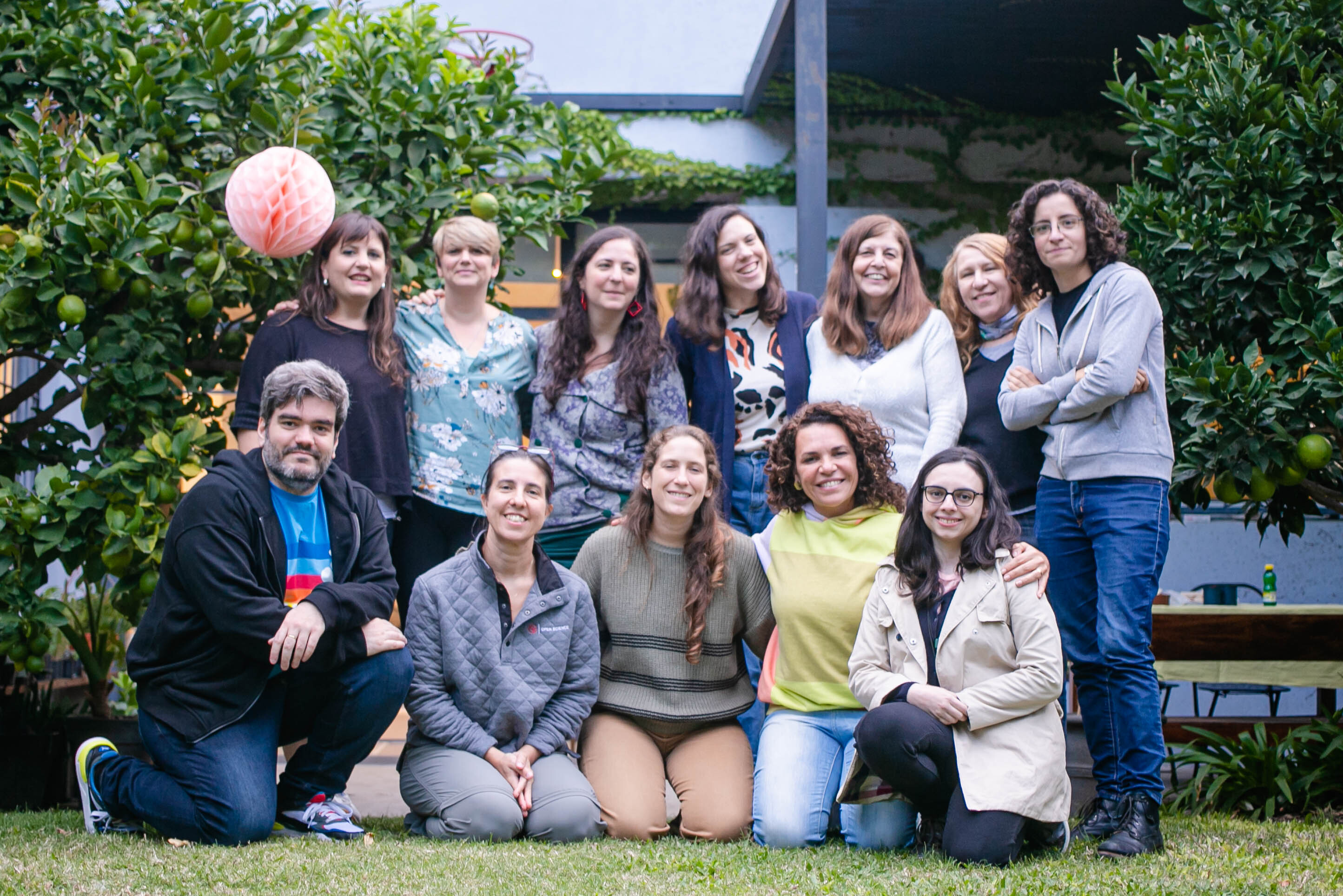 En la imagen se ven 12 personas de diversas edades, informalmente vestidas, en un jardin natural, sonrientes y felices.